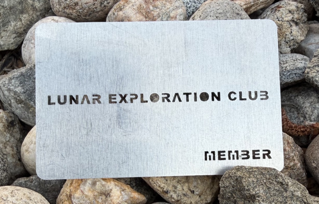 Stainless steel Lunar Exploration Club member card resting on rocks